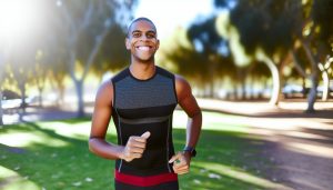 Une personne souriante en tenue de sport, en train de courir dans un parc.